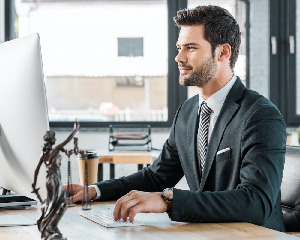 handsome lawyer working with computer at table in office, themis statue on tabletop